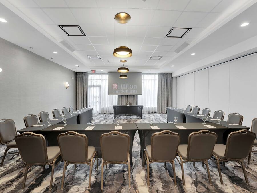 Una sala conferenze con un lungo tavolo, diverse sedie e un grande schermo che mostra il logo Hilton Garden Inn.