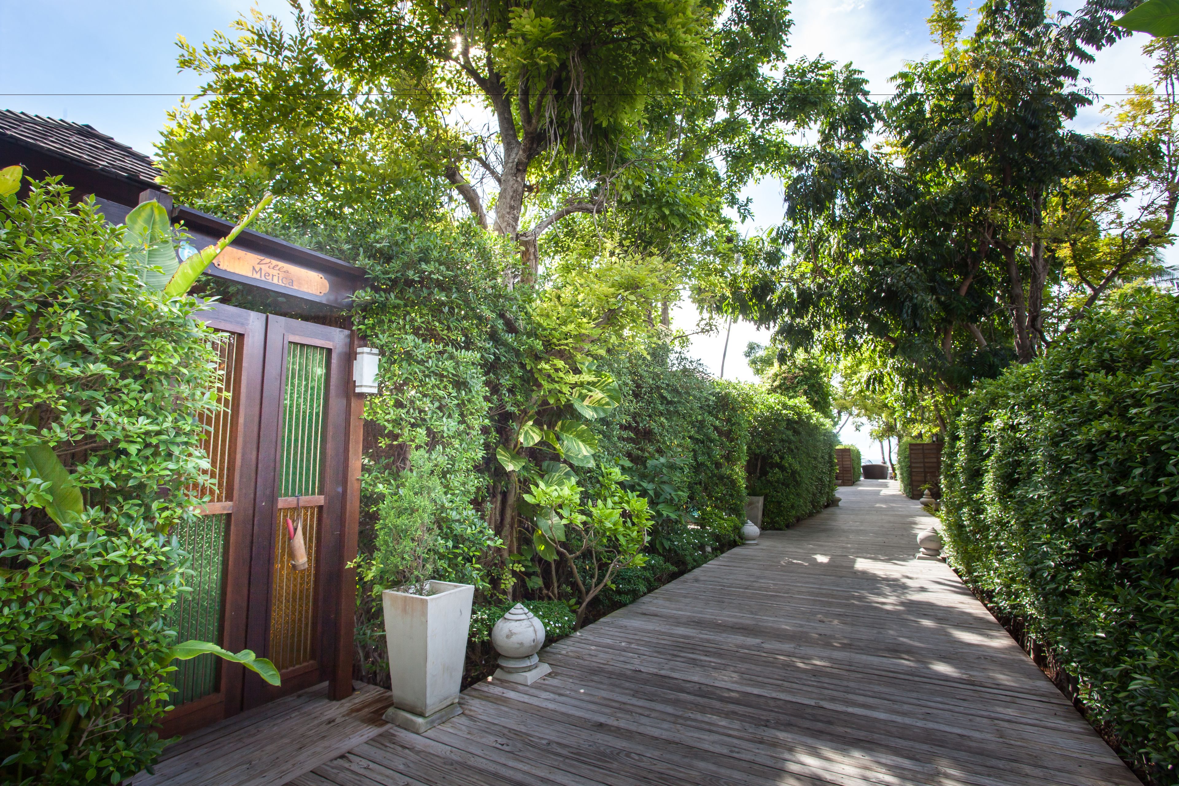 A wooden pathway flanked by lush greenery and a wooden structure with a green door.