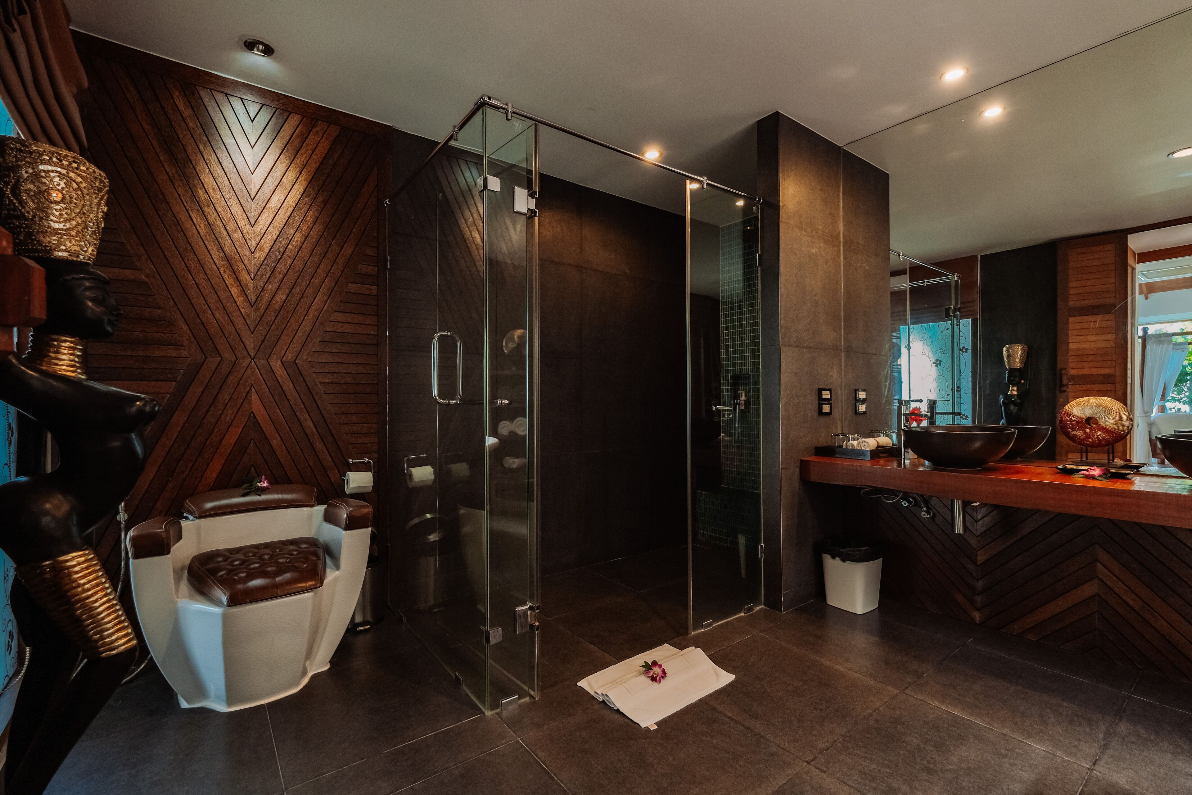 A modern bathroom with a glass-enclosed shower, a wooden vanity with a bowl sink, and a massage chair.