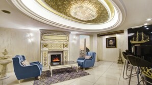 Una sala de estar lujosa con chimenea, dos sillones azules, una mesa de centro y una araña.