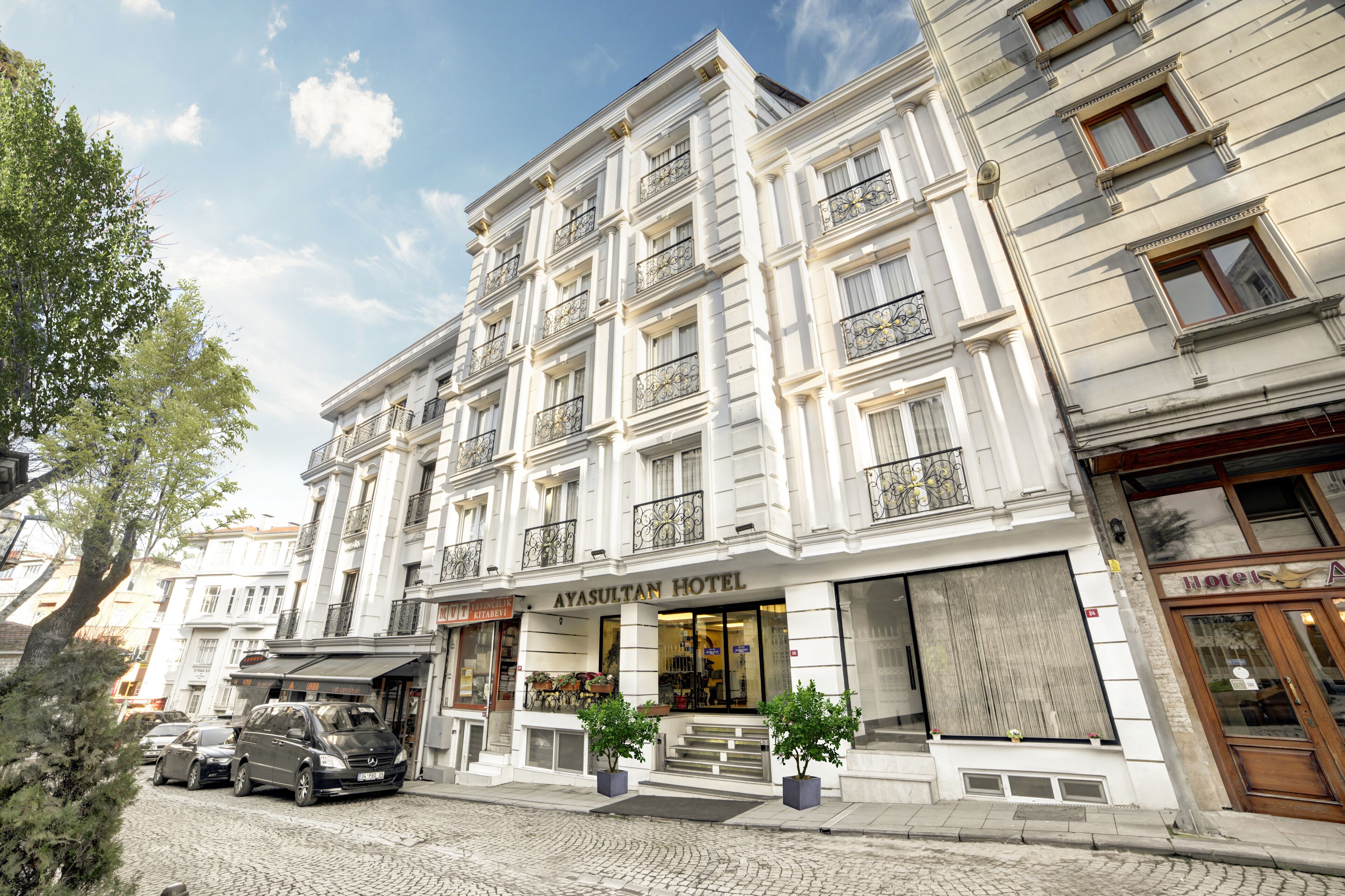 A multi-story hotel with a classic architectural style, featuring balconies with wrought iron railings and a central entrance with steps leading up to the door.