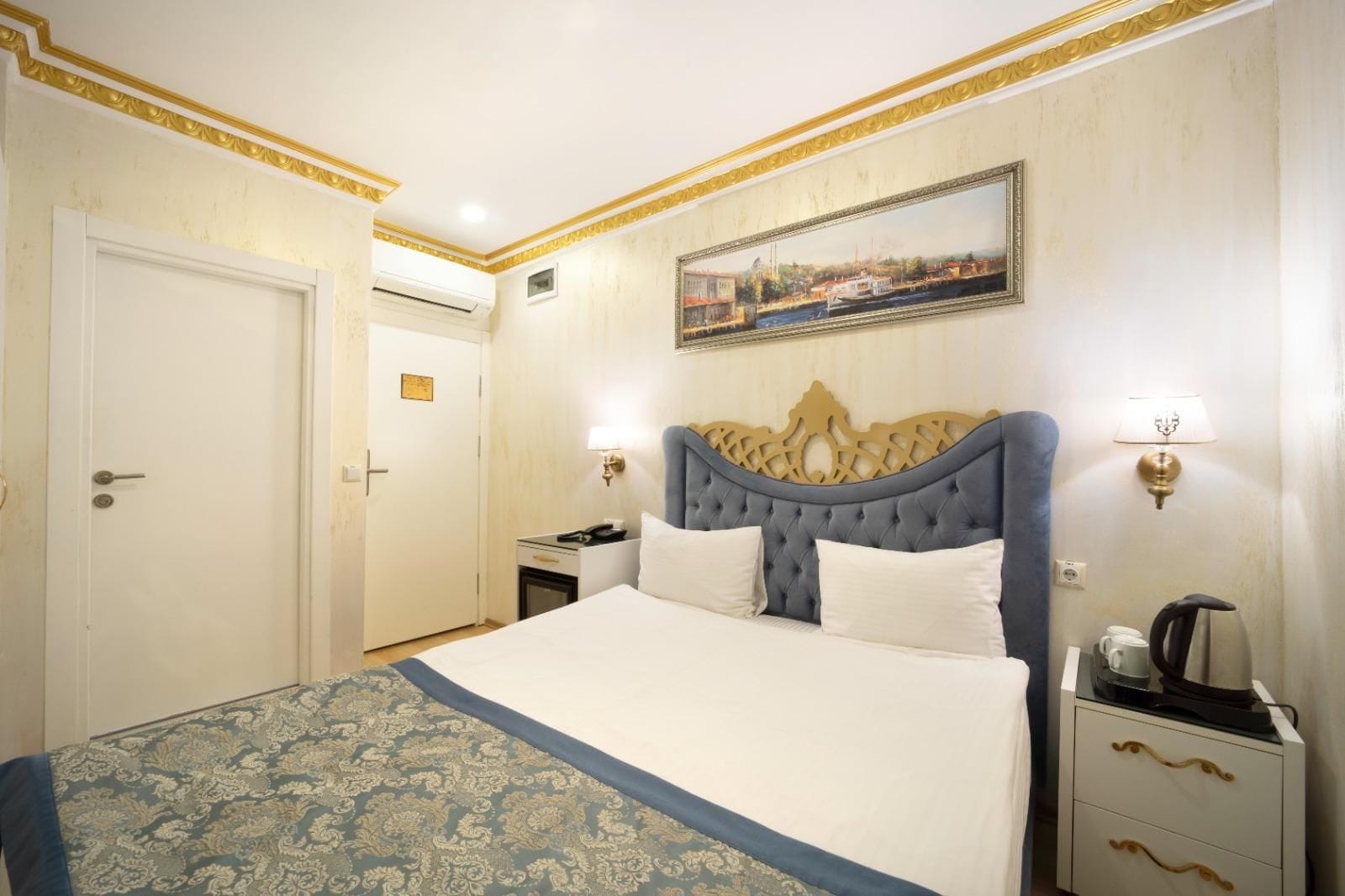 Una habitación de hotel con una cama grande, una mesita de noche, un cuadro en la pared y una puerta.
