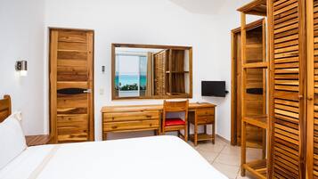 Un dormitorio con un escritorio de madera, una silla, una cama, un televisor y un amplio ventanal con vista al mar.