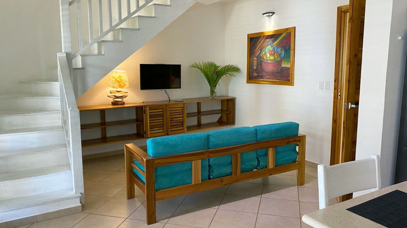 Eine Treppe führt zu einem Wohnbereich mit einer hölzernen Bank, einem Fernseher und einem Bild an der Wand.
