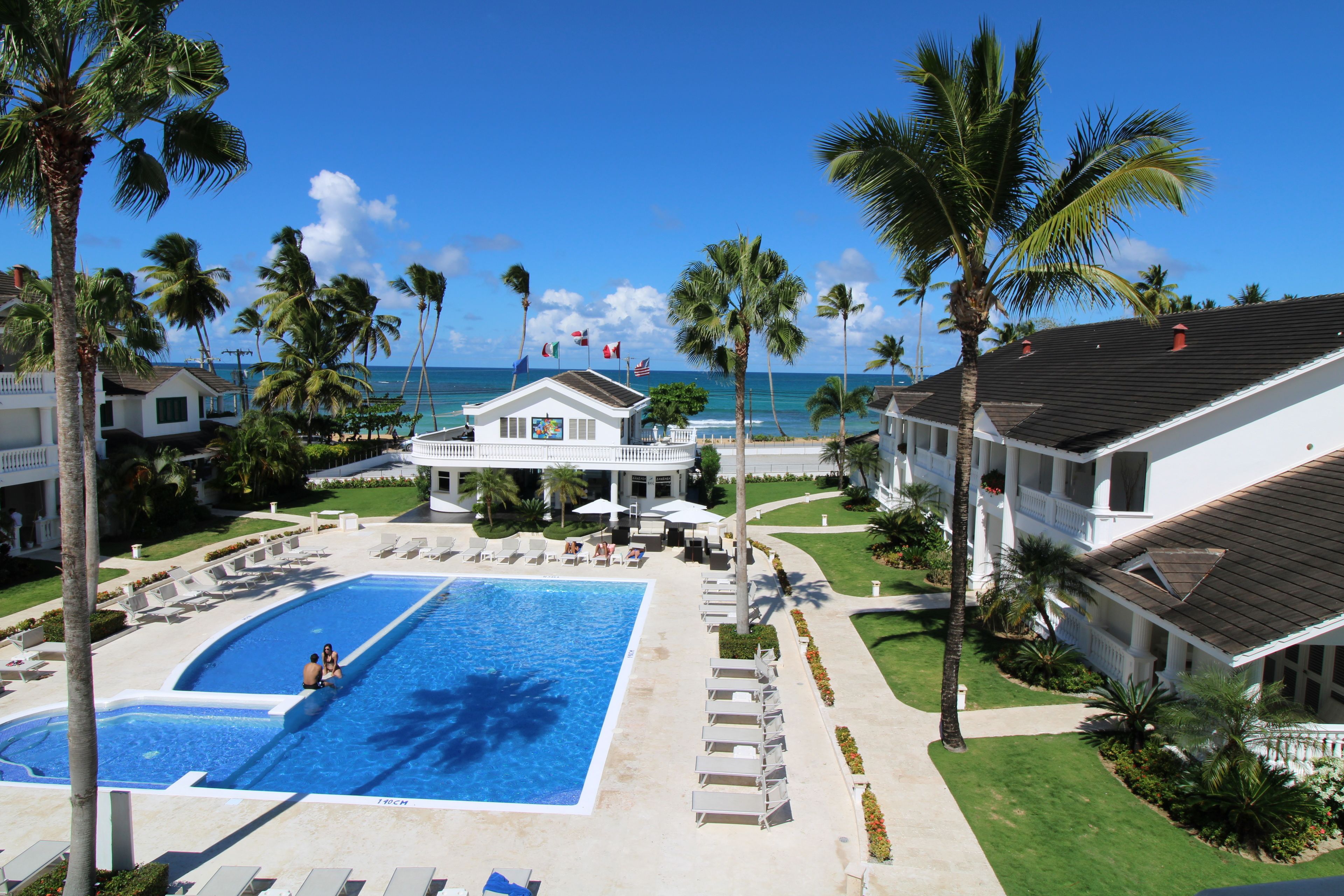 Een resort met een groot zwembad, palmbomen en uitzicht op de oceaan.