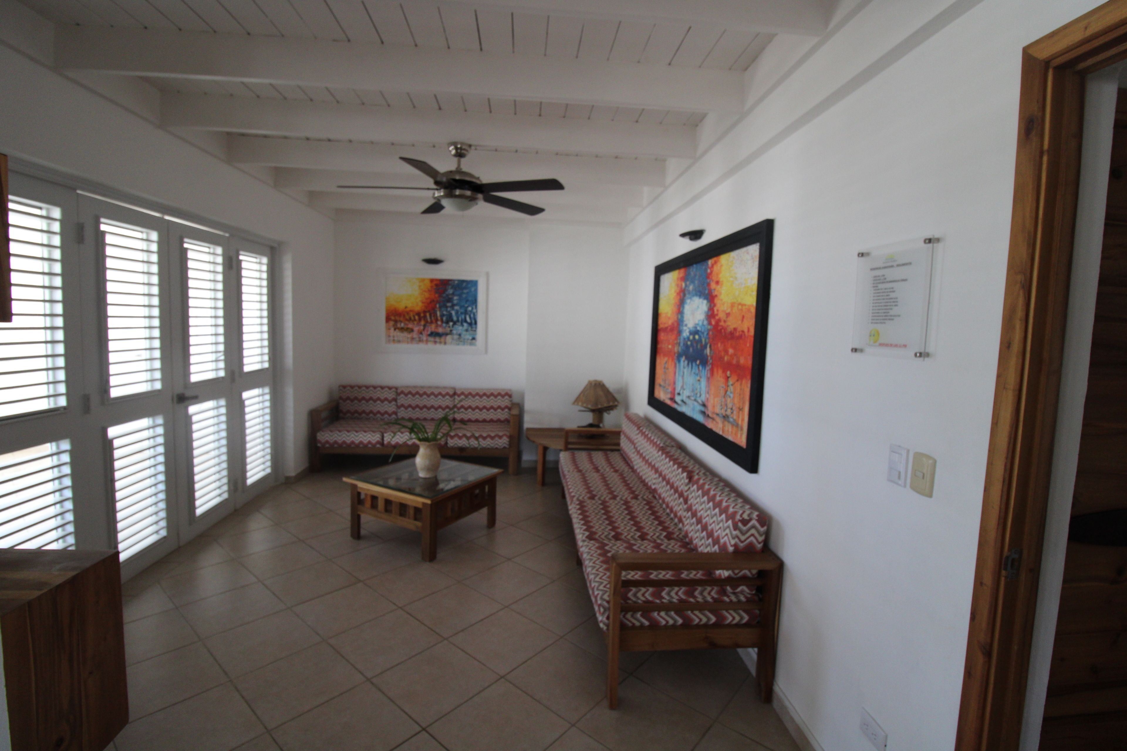 A spacious living area with a ceiling fan, two sofas, a coffee table, and a painting on the wall.