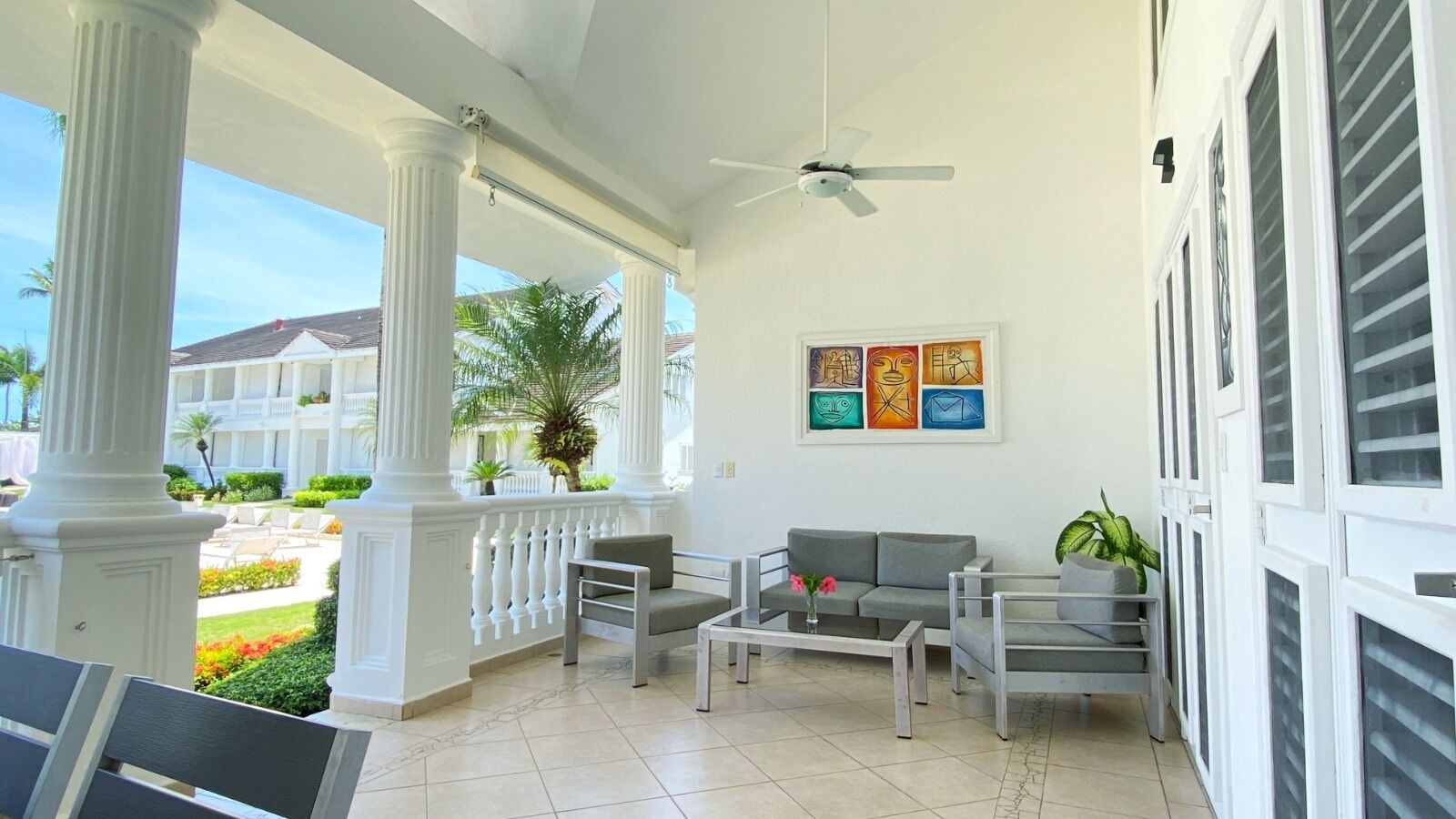 A covered outdoor seating area with white columns, a ceiling fan, and a view of a building with balconies.