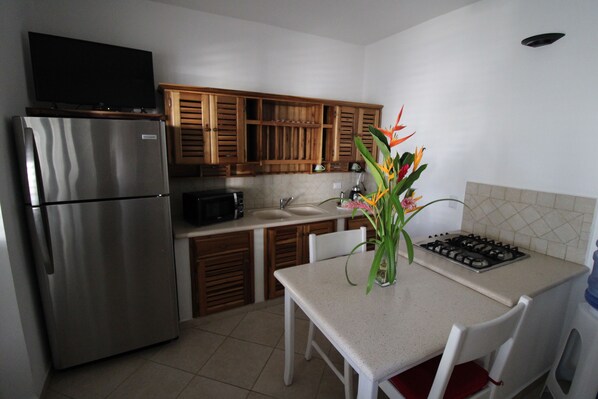 A kitchen with a stainless steel refrigerator, wooden cabinets, a microwave, a sink, and a gas stove. There is a table with chairs and a vase with flowers. - Albachiara Hotel (Las Terrenas)