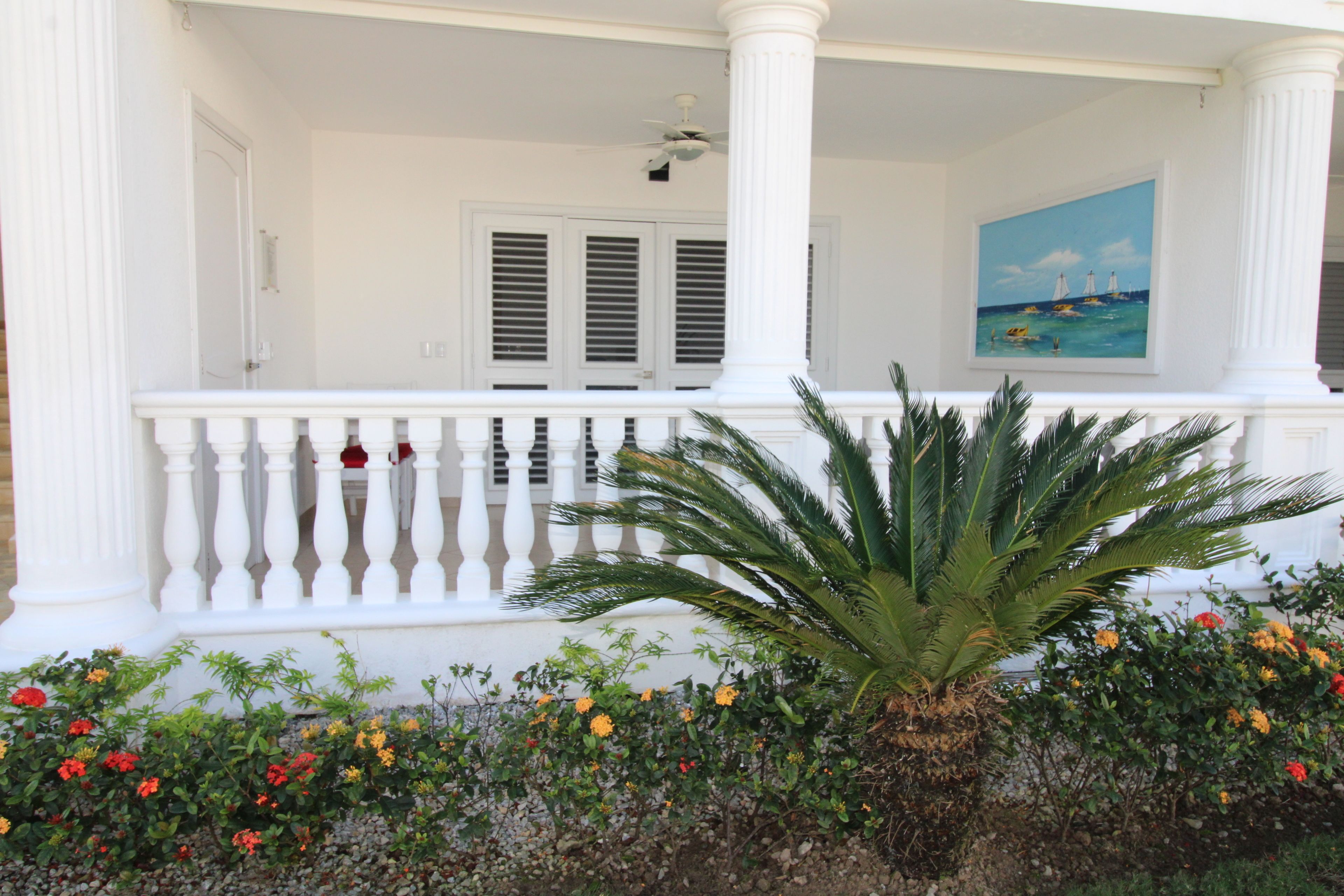A white porch with a balustrade, a palm tree, and colorful flowers.