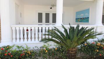 A white porch with a balustrade, a palm tree, and colorful flowers.
