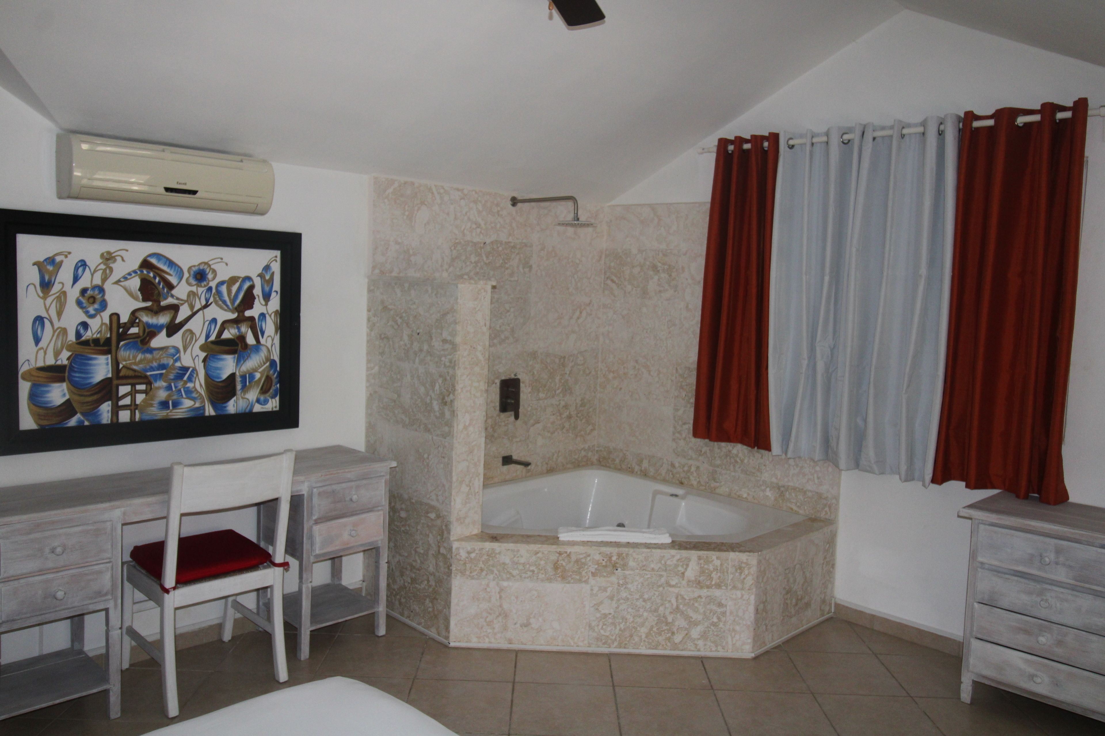 A bathroom with a bathtub, a shower, a desk with a chair, and a painting on the wall.