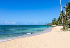 A beach with clear turquoise water, sandy shore, and palm trees. - Albachiara Hotel (Las Terrenas)