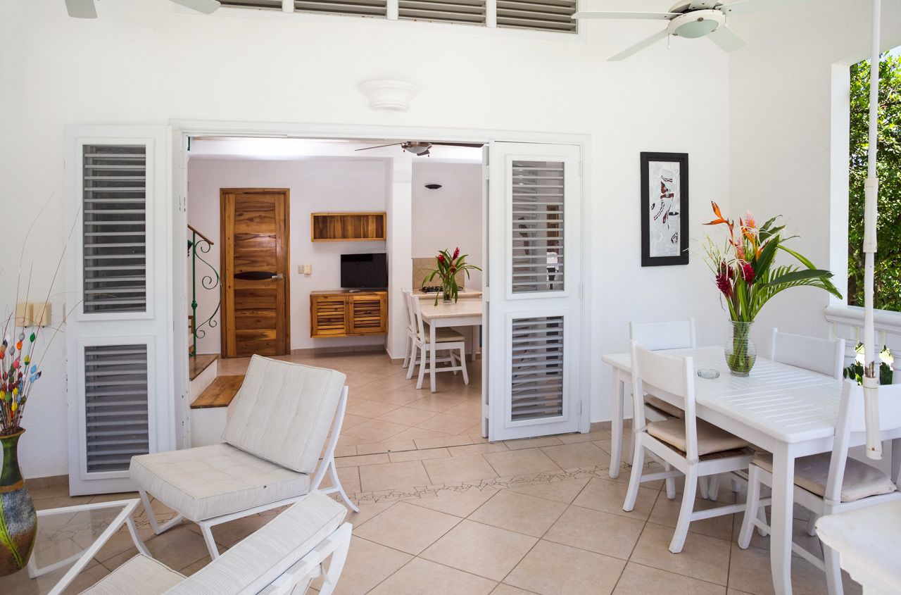 A spacious living area with a white sofa, a dining table with chairs, and a kitchen area in the background.