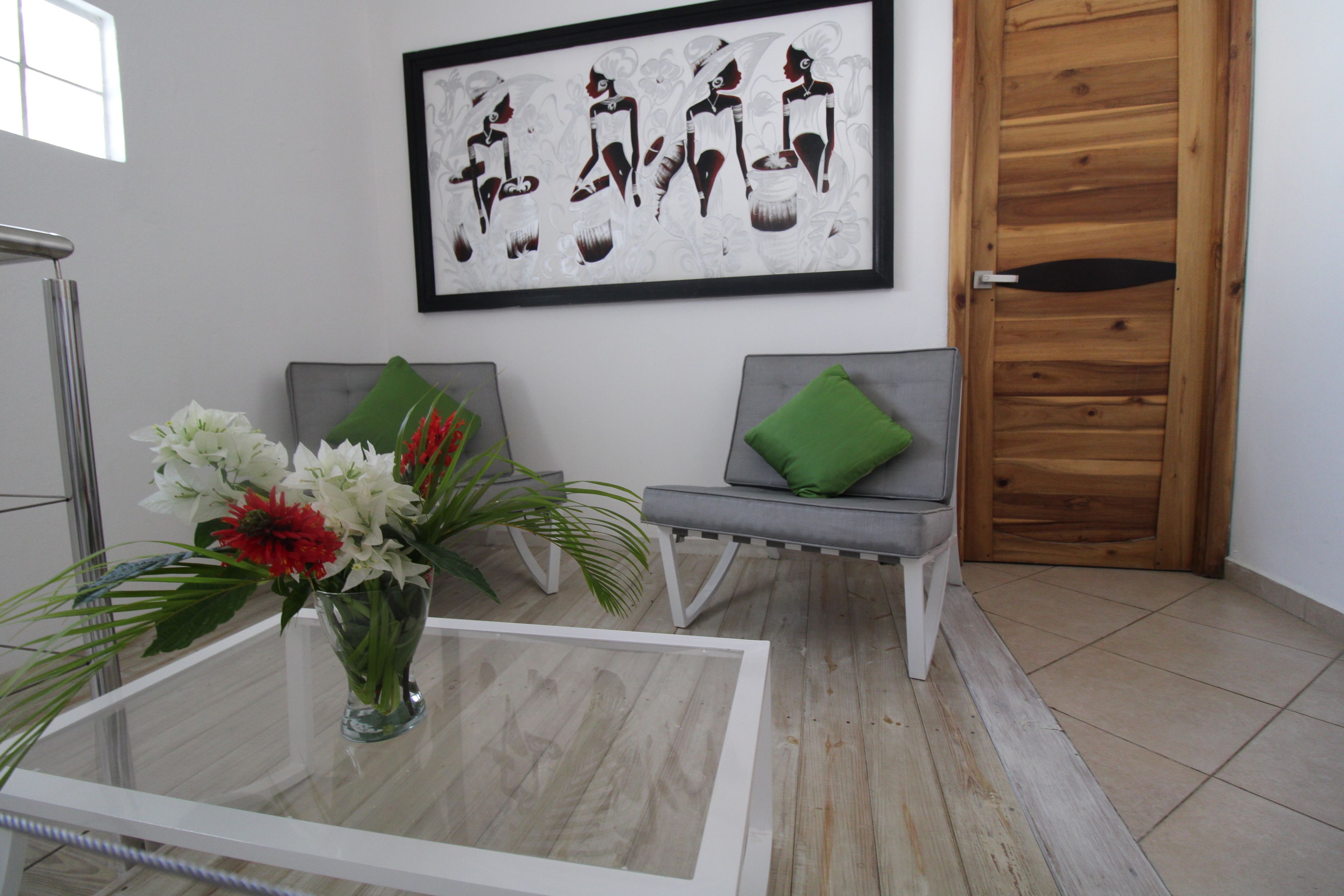 Une pièce moderne avec une table basse en verre, un canapé gris agrémenté d’un coussin vert et une œuvre d’art encadrée au mur.