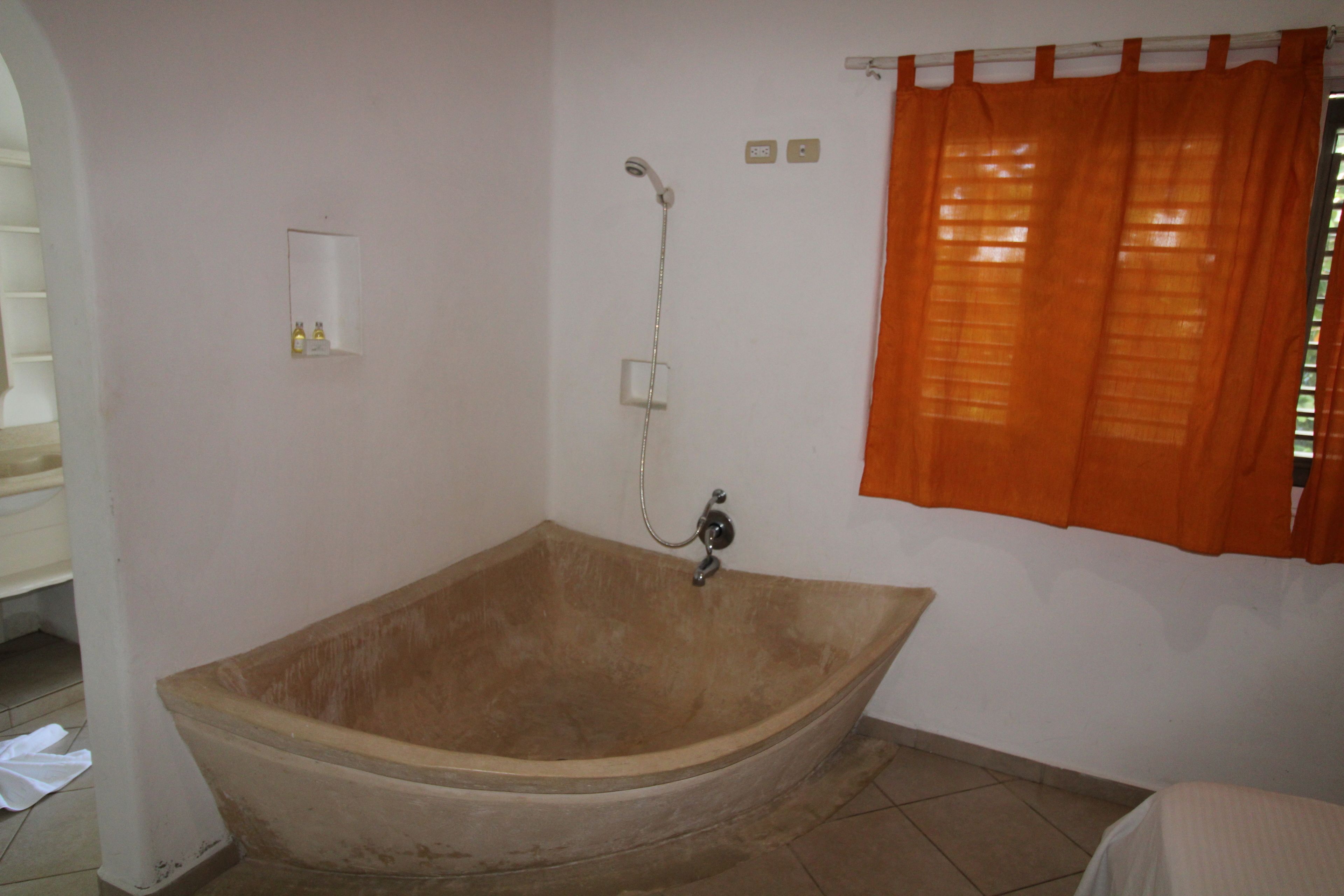Un baño con bañera, ducha y ventana con cortinas anaranjadas.