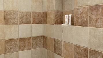 Ducha con cabezal de ducha de mano y grifo empotrado. El espacio de la ducha tiene azulejos color beige y marrón.