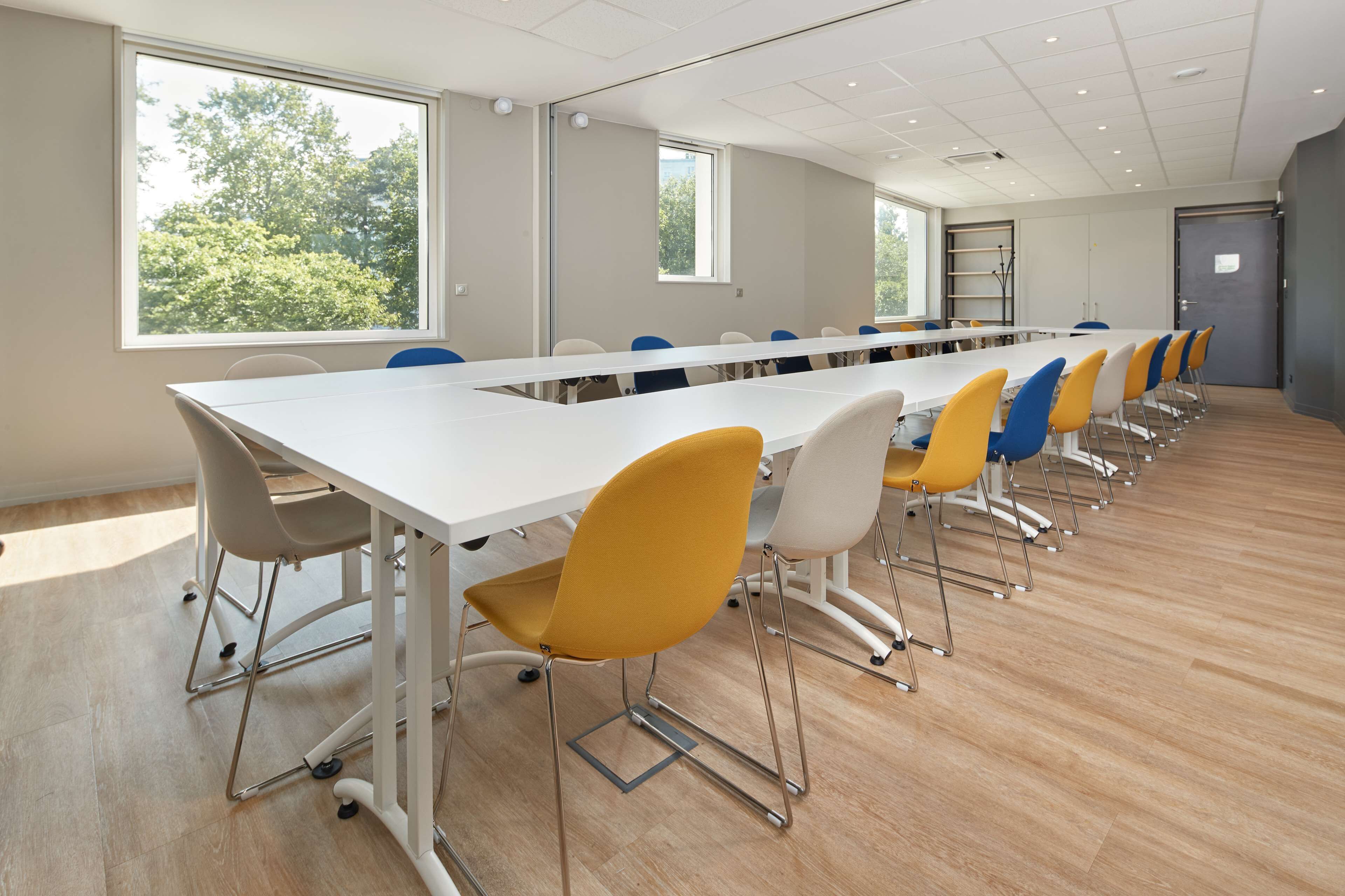 Ein Konferenzraum mit einem langen Tisch, Stühlen, großen Fenstern und einer Tür.