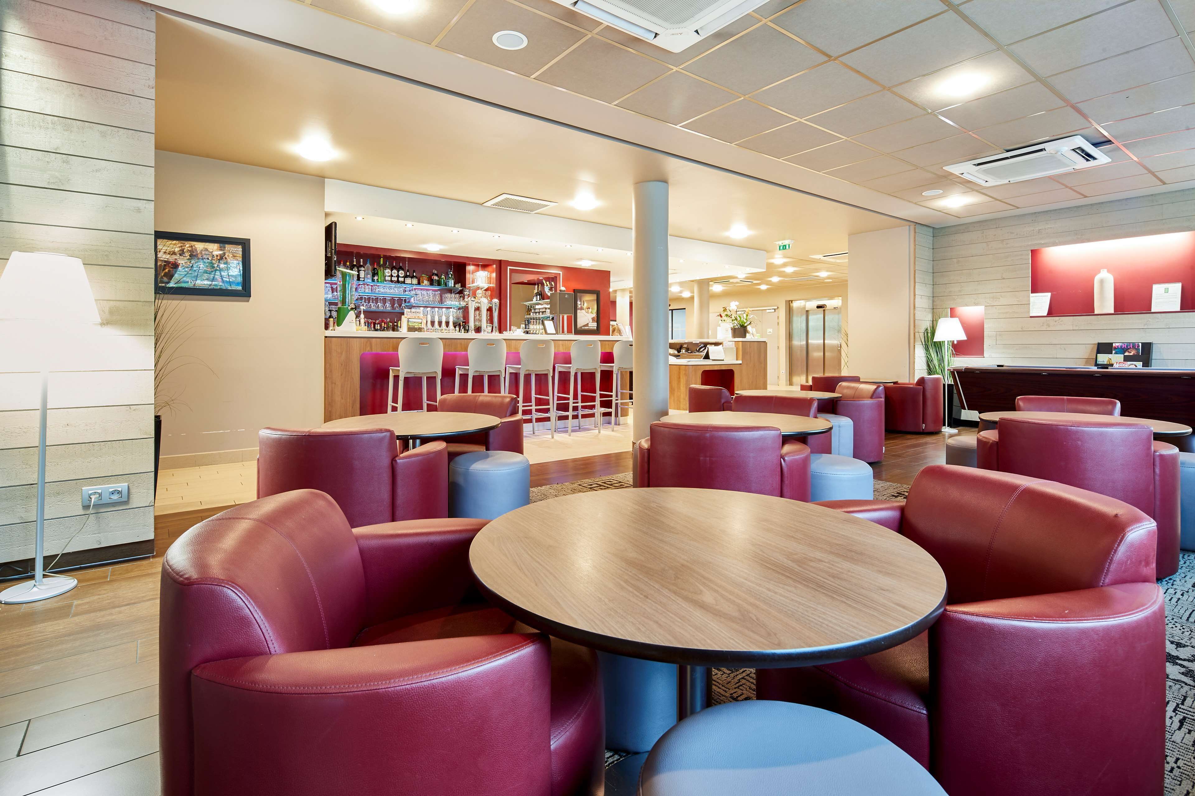 Et moderne loungeområde med runde borde og røde læderstole, en bar med barstole og en reception.