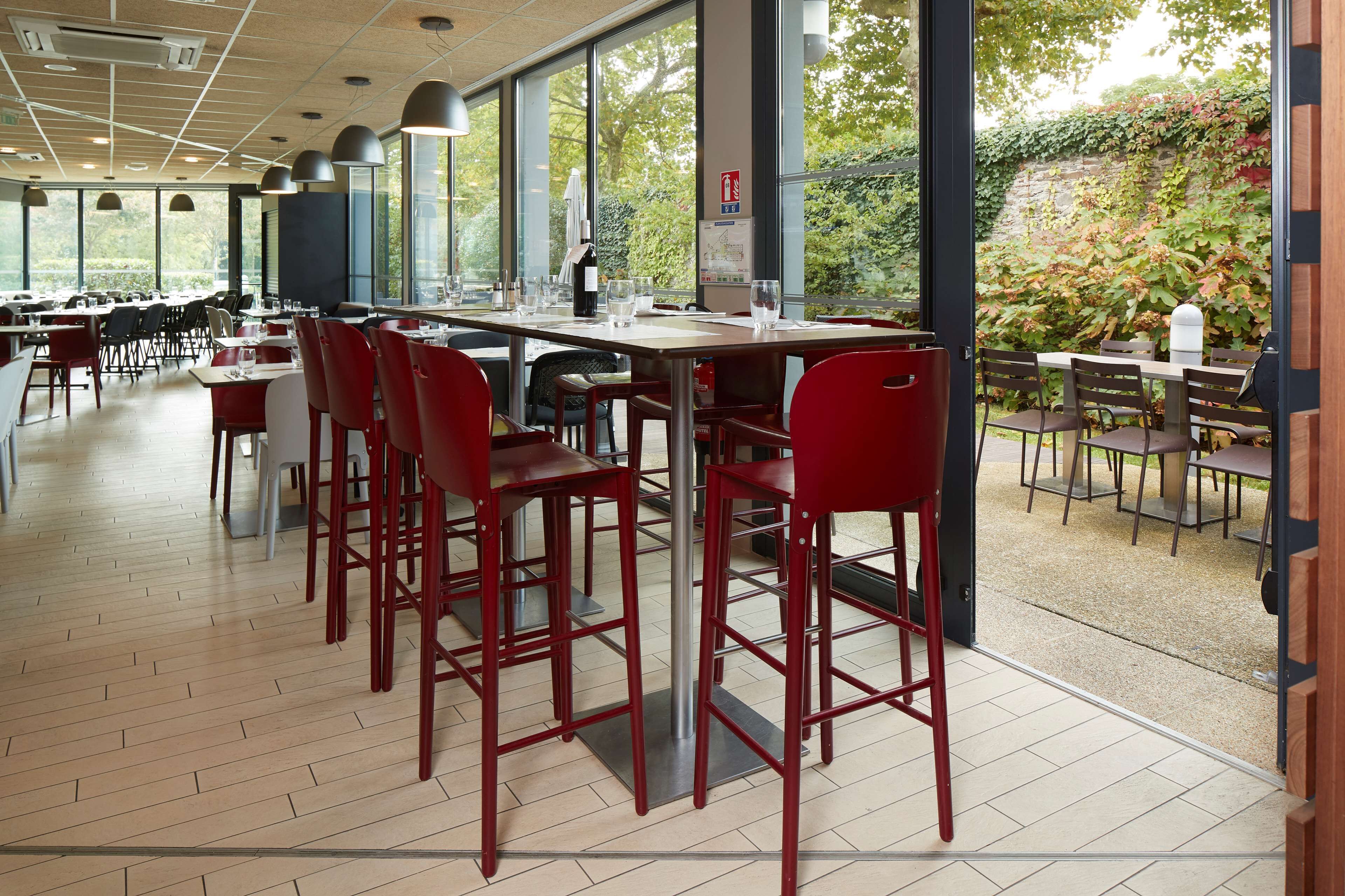 Un vaste espace dédié à la salle à manger, avec de grandes tables et des chaises rouges, de grandes fenêtres offrant une vue sur la verdure, et un extincteur fixé au mur.