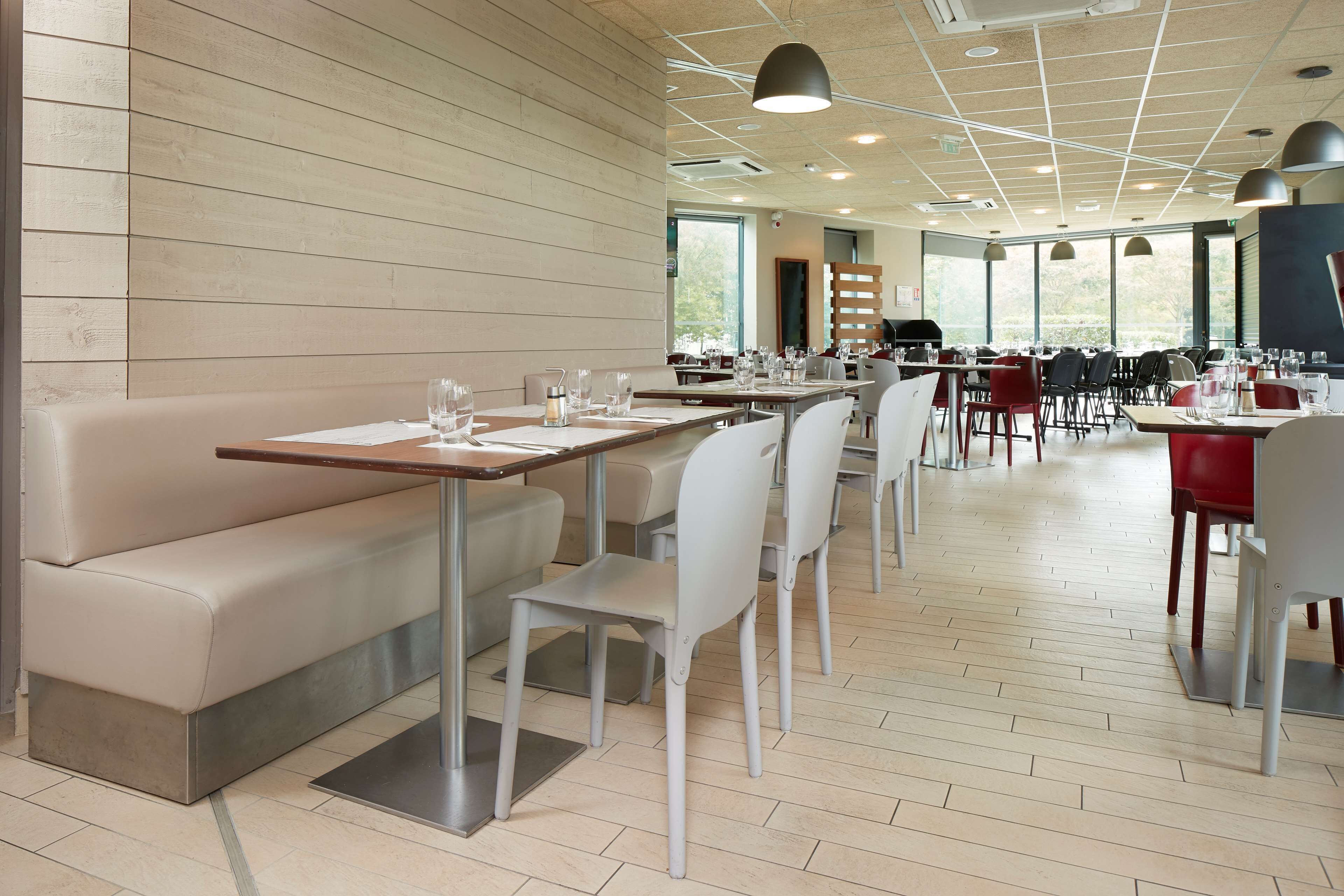 A modern restaurant with a clean, minimalist interior, featuring a mix of seating options including a long communal table and individual booths, with a view of the outdoors through large windows.
