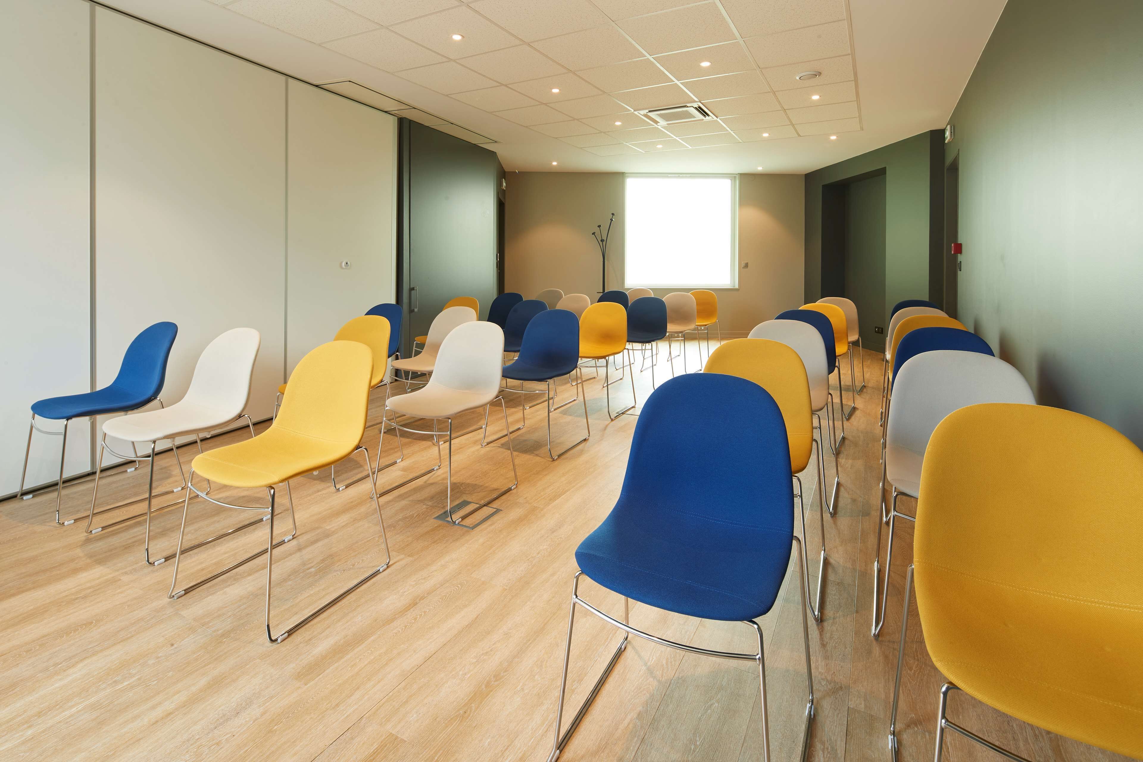 A conference room with rows of chairs in various colors, a large window, and a wooden floor.