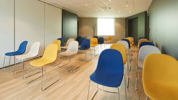 A conference room with rows of chairs in various colors, a large window, and a wooden floor.