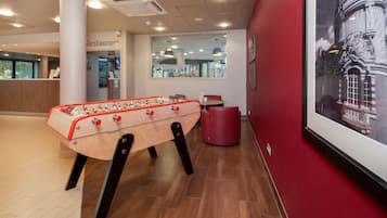 A foosball table in a modern lobby with a red wall and a framed historical building photo.