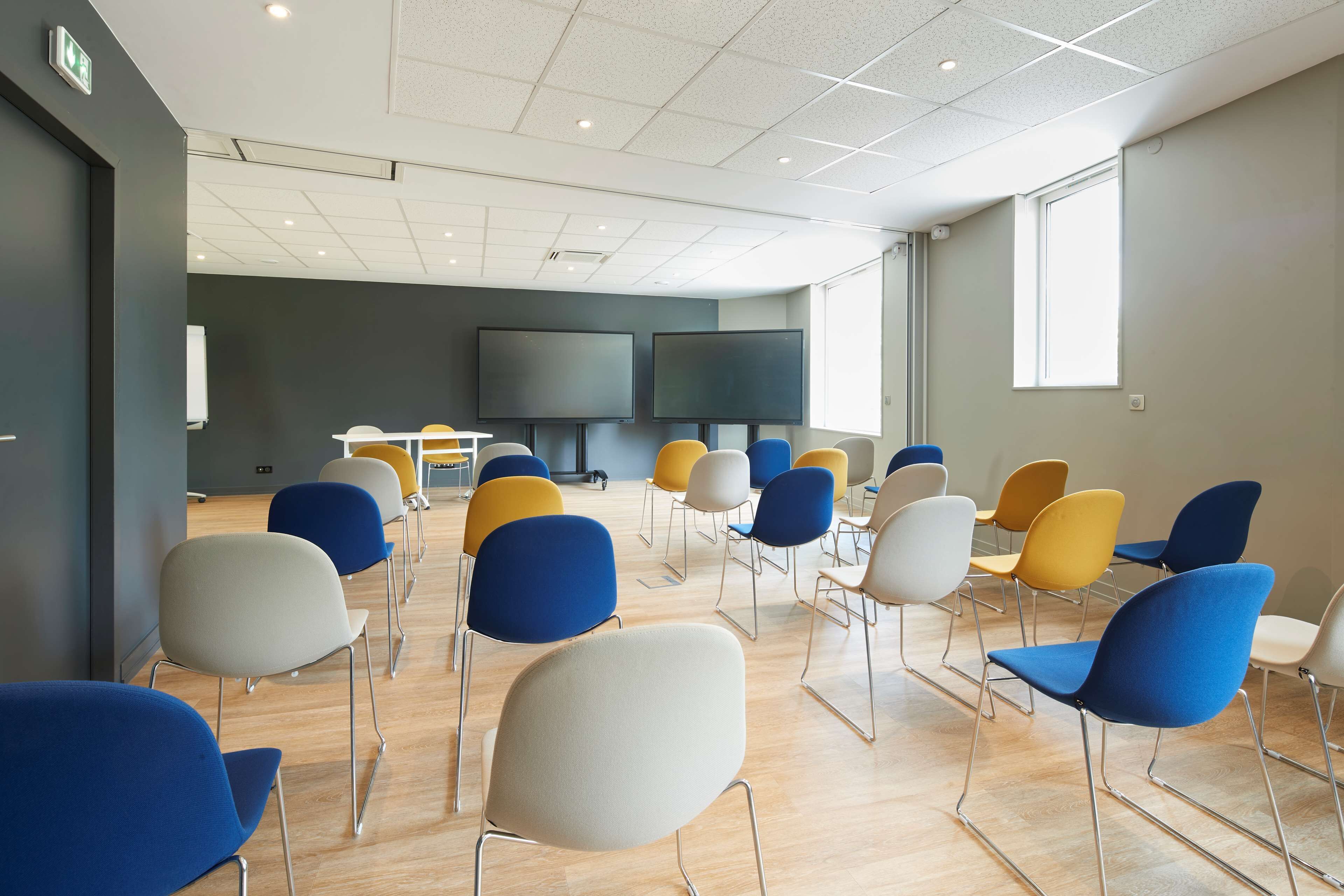 Una sala de conferències amb files de cadires, una pantalla gran i una finestra.