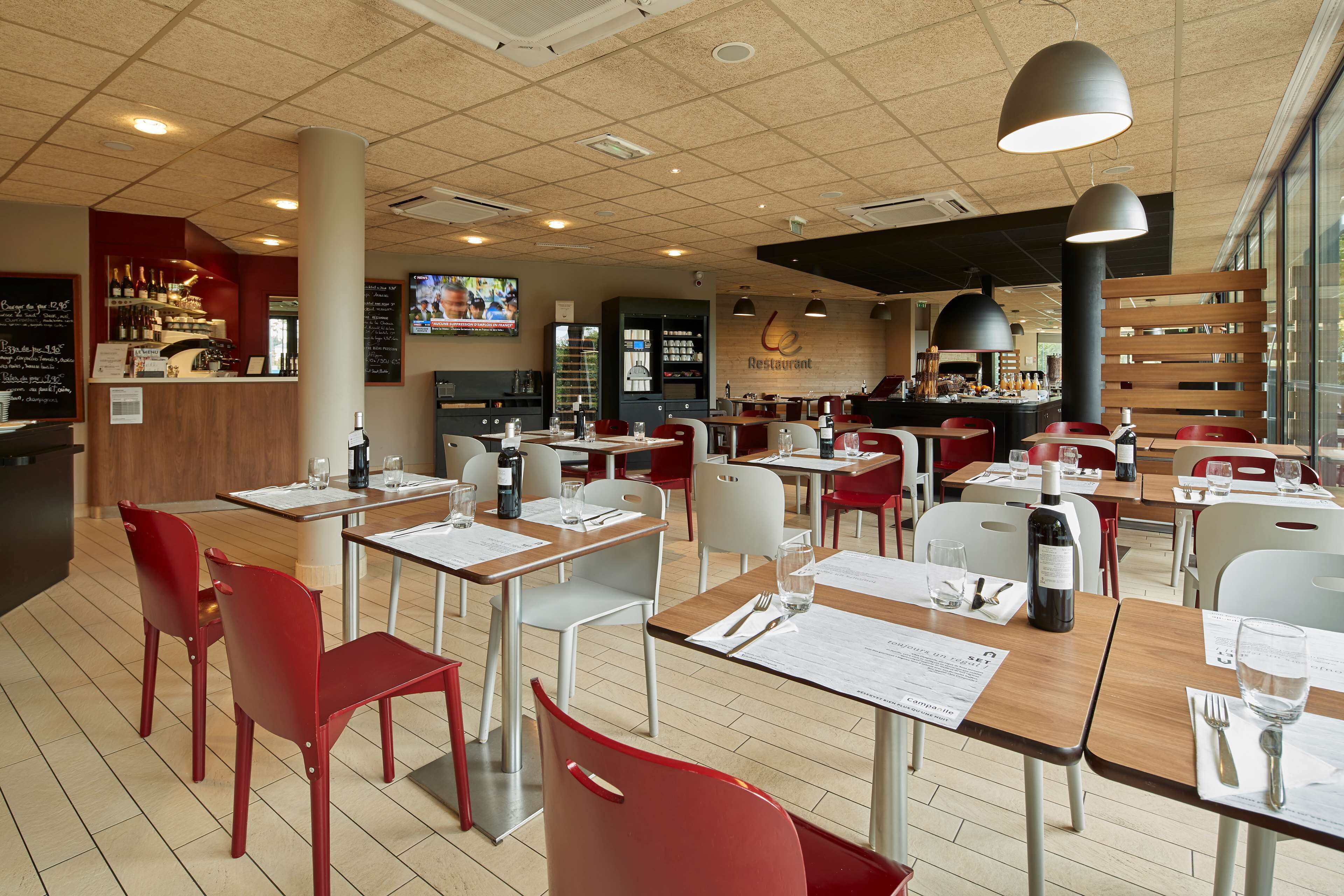 A restaurant with multiple tables and chairs, a counter with a menu, and a television screen.