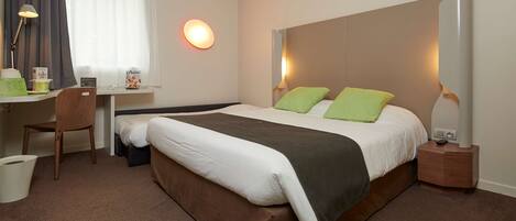 Una habitación de hotel con cama, escritorio, silla y lámpara fijada a la pared.