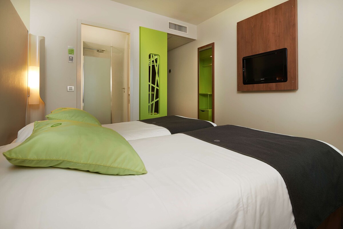 A hotel room with two beds, a green door, a television mounted on the wall, and a shower area.