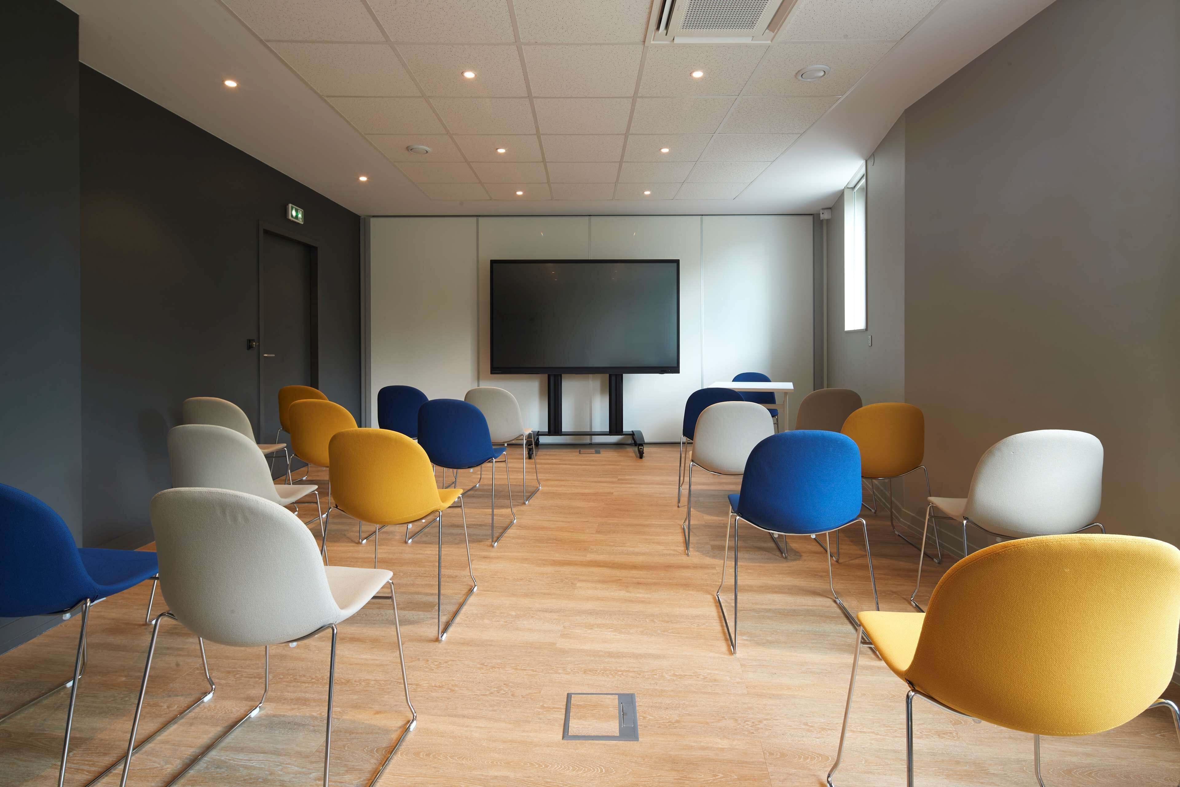 Una sala conferenze con un grande schermo, diverse sedie e un pavimento in legno.