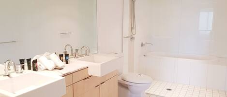 A modern bathroom with a double sink vanity, a toilet, and a shower area.