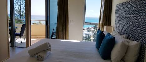 A hotel room with a large bed, a view of the sea, and a balcony with outdoor furniture.