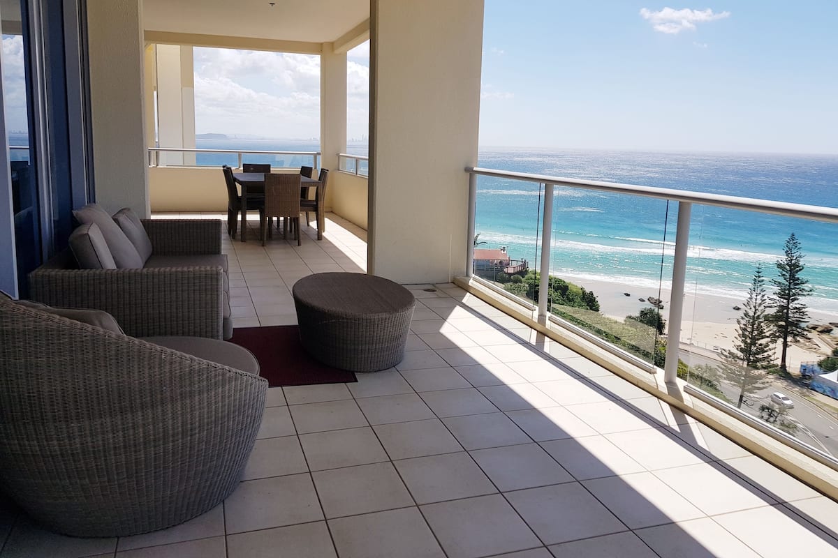 A balcony with a view of the ocean, wicker furniture, and a dining table.