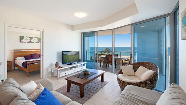 Un salon moderne avec un lit, une télévision et un balcon offrant une vue sur l’océan.