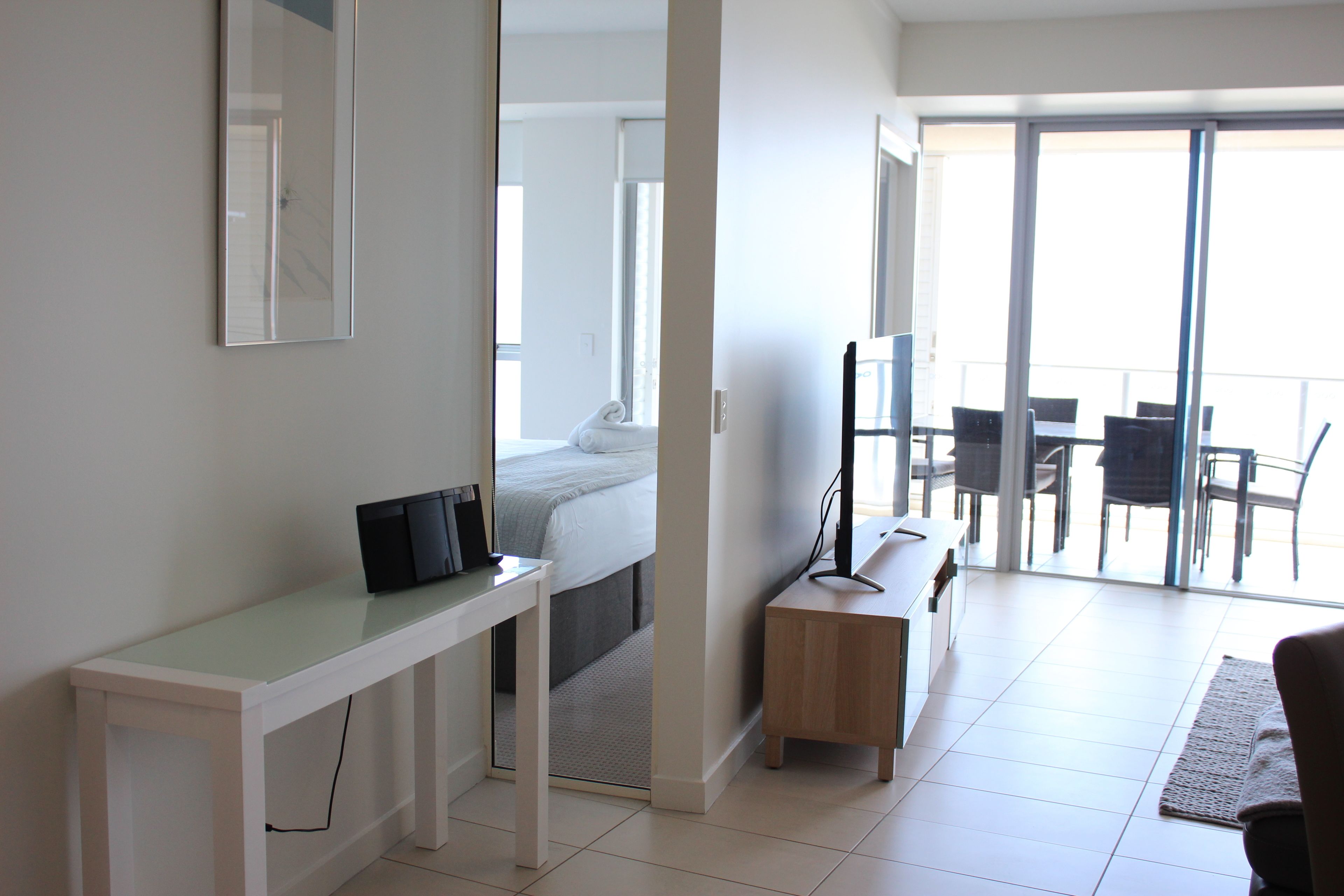 A modern hotel room with a bed, a desk with a computer, a TV, and a balcony with chairs.