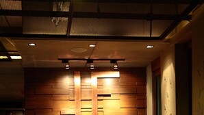 A reception area with a wooden panel wall, a pink-lit counter, and a floor with a yellow sign. - The Fusion Suites (Bangkok)