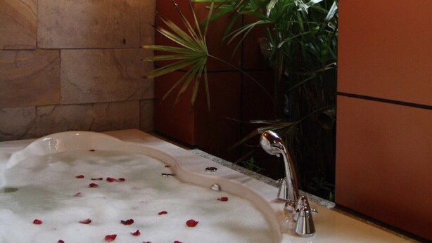 A bathtub filled with bubbles and rose petals, a marble countertop, and a modern faucet. - The Fusion Suites (Bangkok)