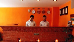 A reception desk with two staff members, a clock, and a reception sign. - Cascade Hotel (Kathmandu)