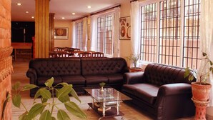 A spacious living room with a dark brown leather sofa, a glass coffee table, and a large window with metal bars. - Cascade Hotel (Kathmandu)