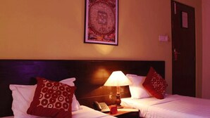 A hotel room with two beds, a nightstand with a lamp, a telephone, and a framed picture on the wall. - Cascade Hotel (Kathmandu)