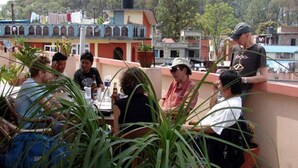A group of people seated at an outdoor table with potted plants, overlooking a residential area with colorful buildings. - Cascade Hotel (Kathmandu)
