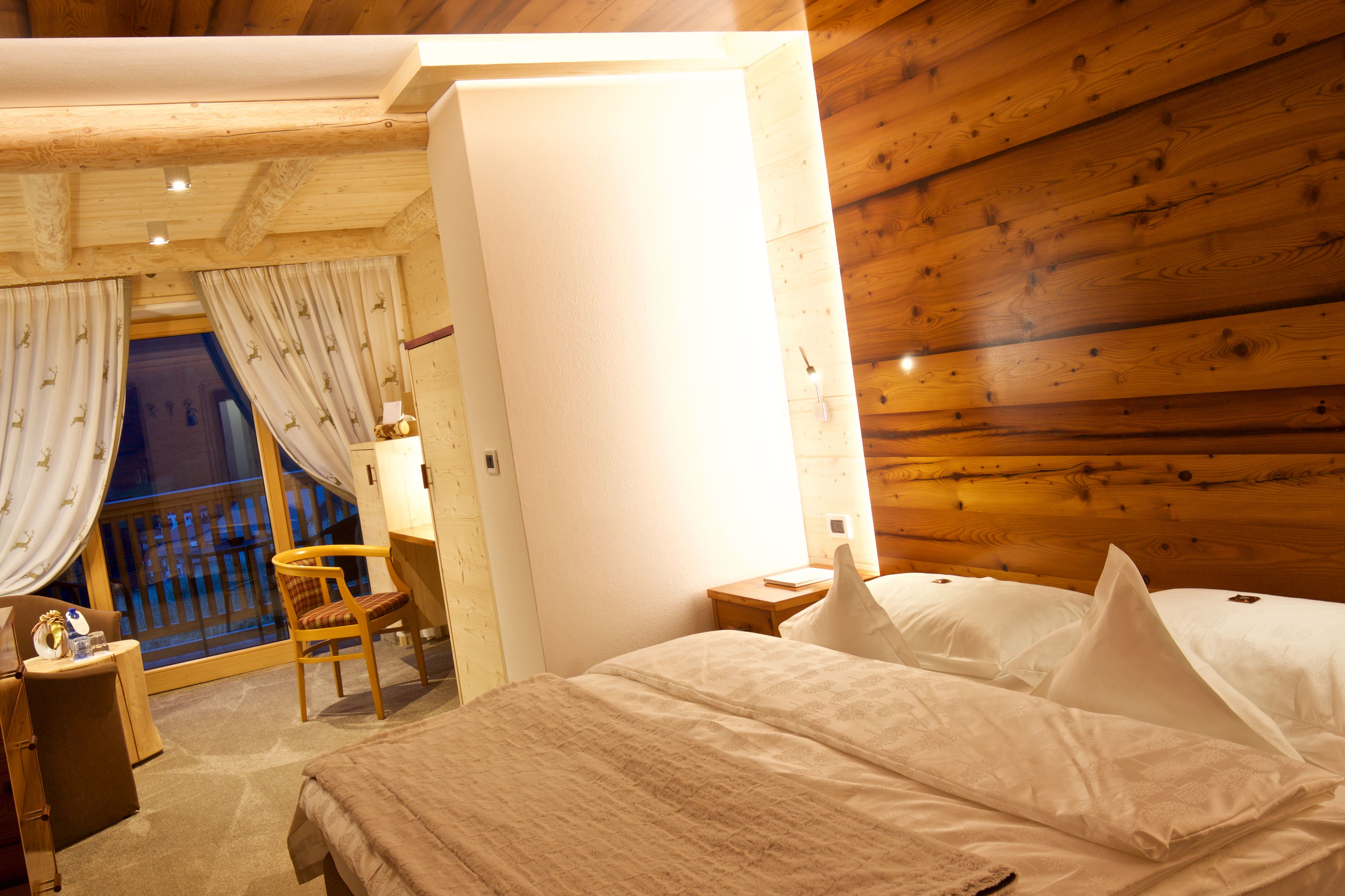 A wooden-paneled room with a bed, a chair, a desk, and a window with curtains.