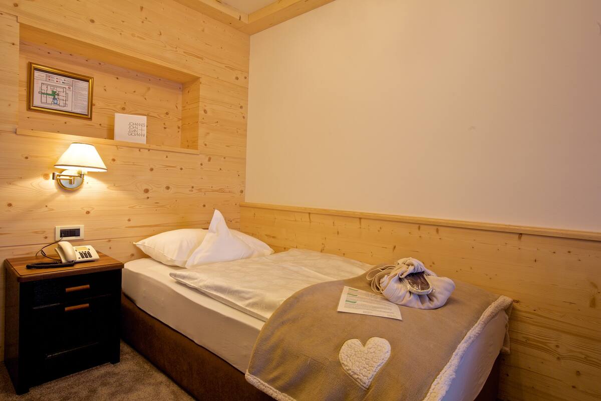 A wooden room with a bed, a nightstand with a lamp, and a framed certificate on the wall.