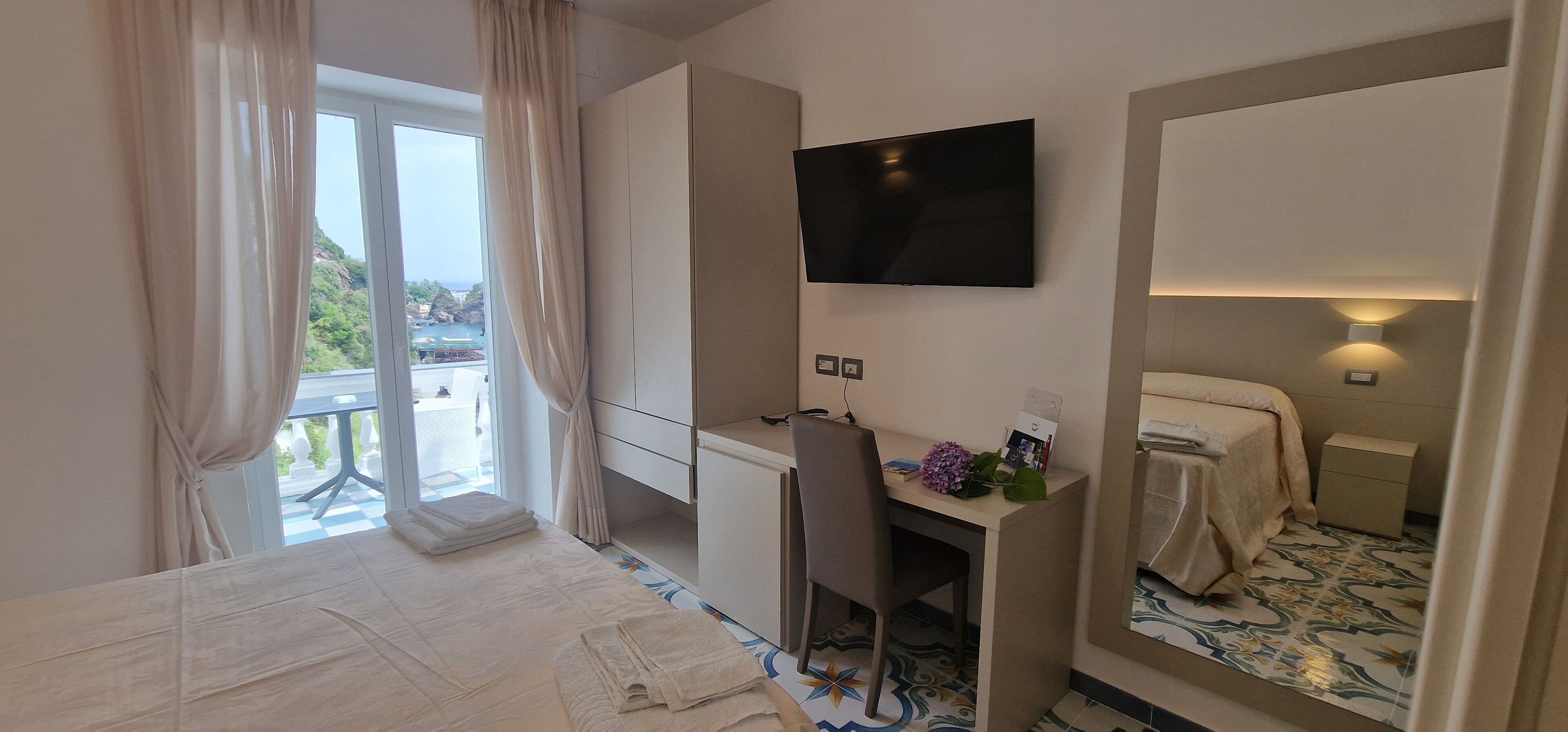 A hotel room with a bed, a desk, a television, and a large window with curtains.