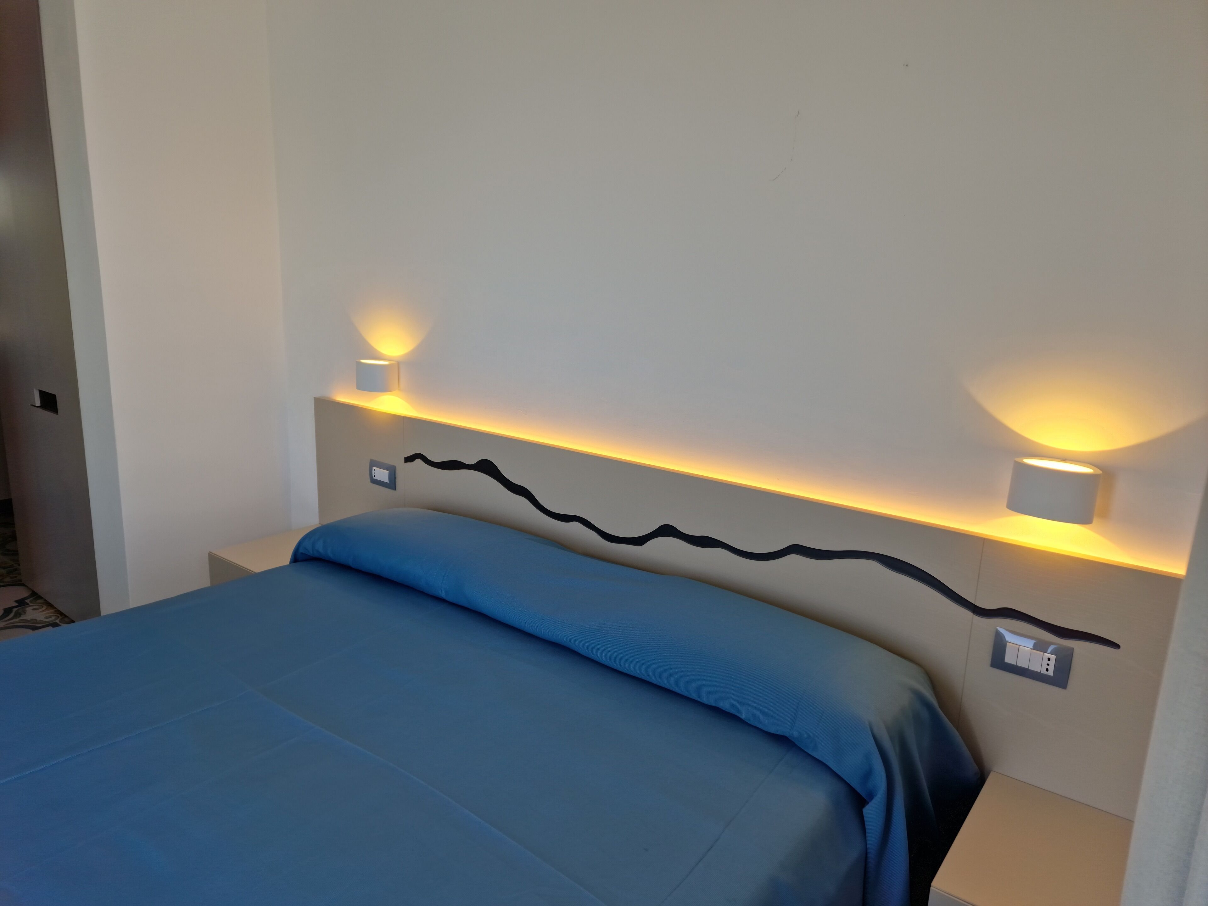 A hotel room with a bed, two bedside lamps, and a wall-mounted light fixture.