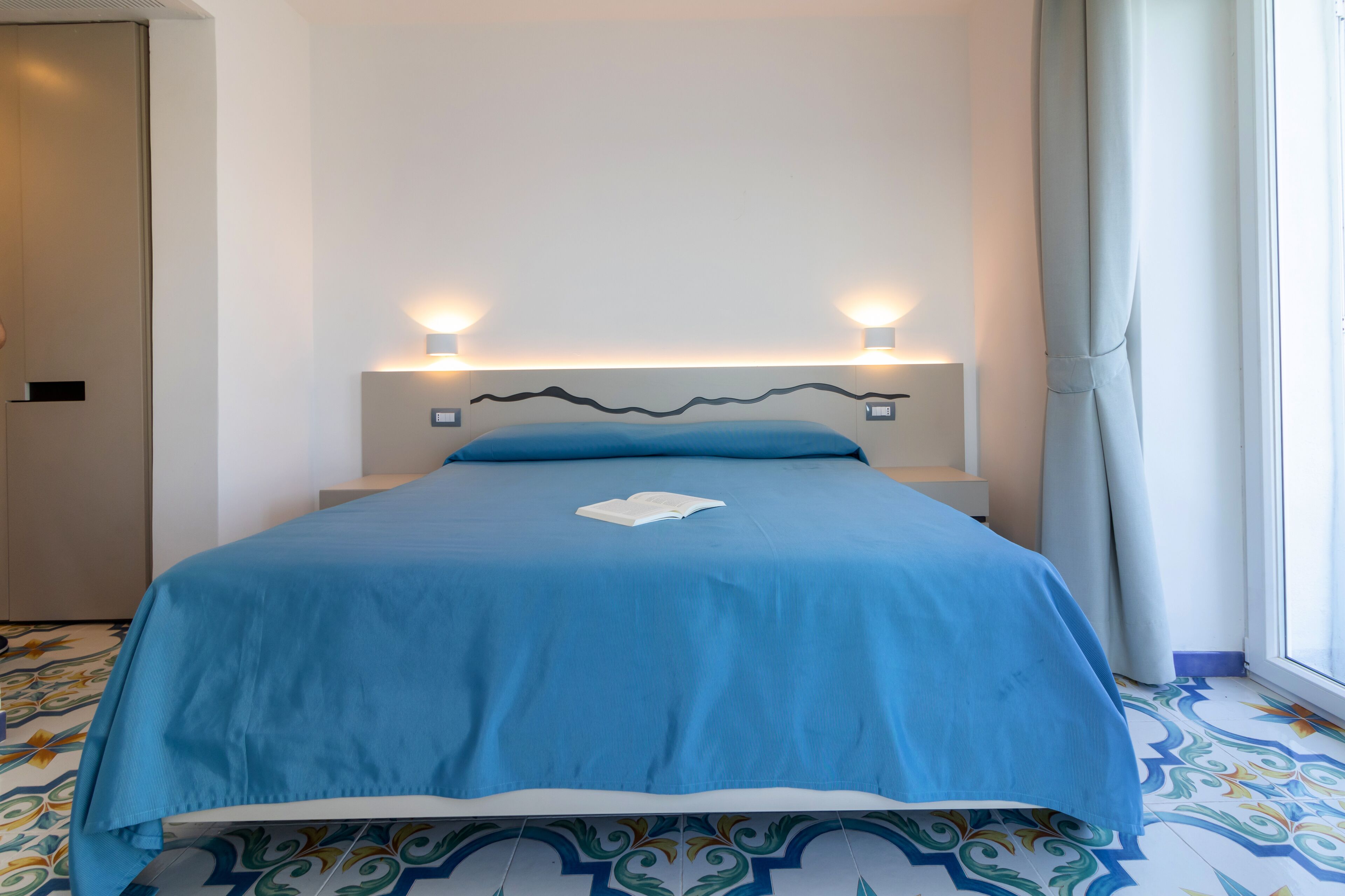 Une chambre d’hôtel avec un lit, une table de chevet et une fenêtre avec des rideaux.