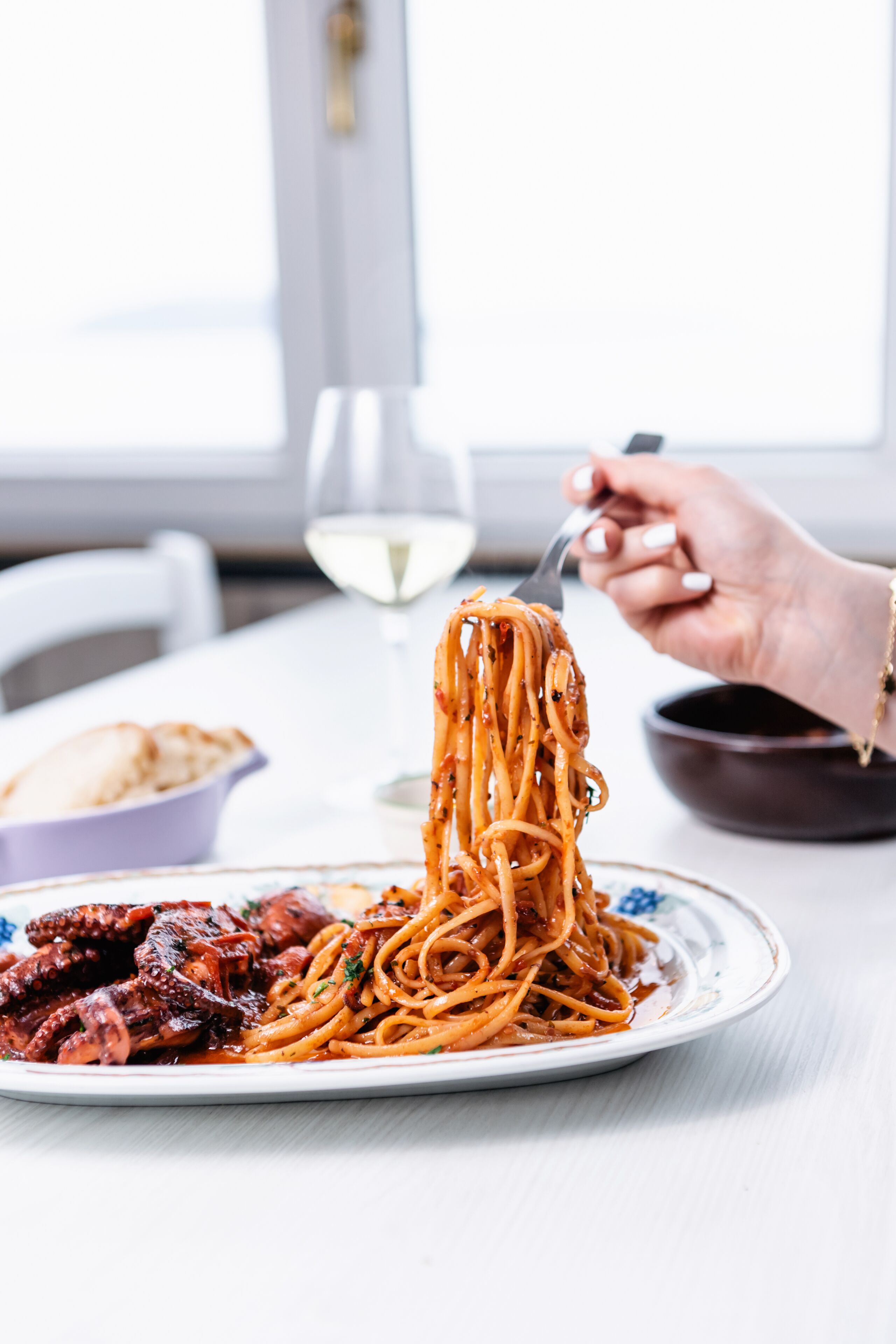 Une assiette de spaghettis à la sauce tomate et à la viande, accompagnée d’un bol de pain.