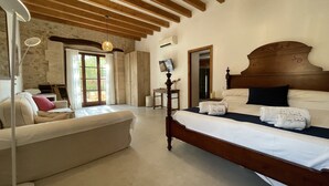 A bedroom with a large bed, wooden ceiling beams, a stone wall, and a modern lamp. - Finca Son Samà (Llucmajor)